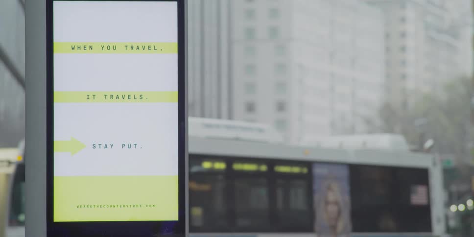 Buses and cars drive down a city street while a sign displays advertising