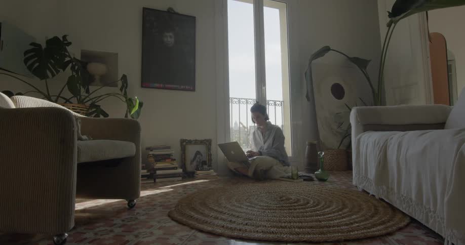 A woman sits on the floor and uses her laptop