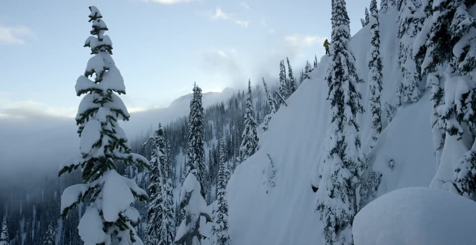 A skier stands on top of a steep slope in winter