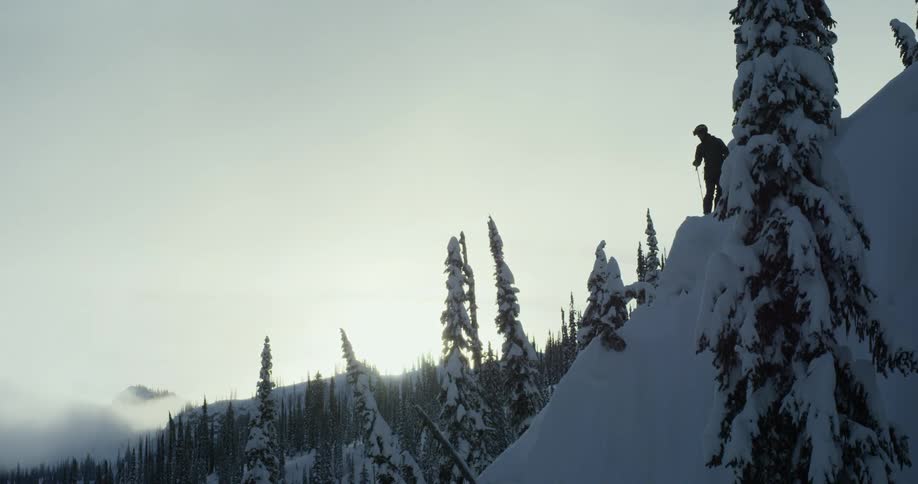 A skier stands on top of a snow covered slope
