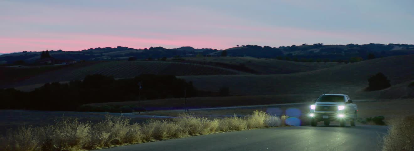 A vehicle drives down a rural road at night