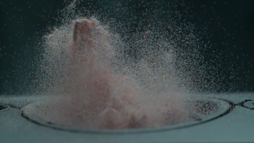 A vibrating speaker throws colored sand and particles into the air