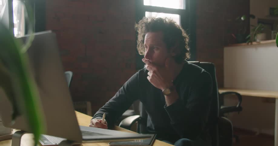 A man sitting at a desk looking at a laptop