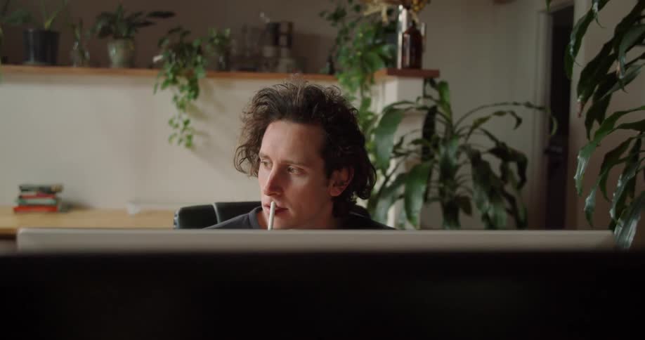 A man sitting before a computer monitor in a room with many potted plants