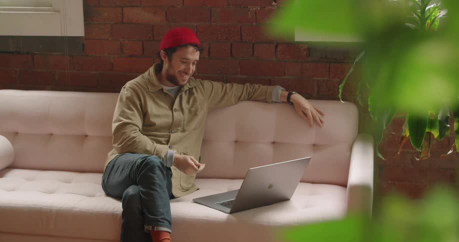 Man sitting on the sofa skypes on laptop and laughs