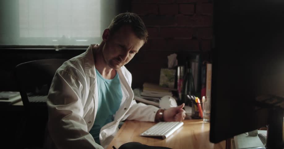 A man in a lab coat looks at a computer screen