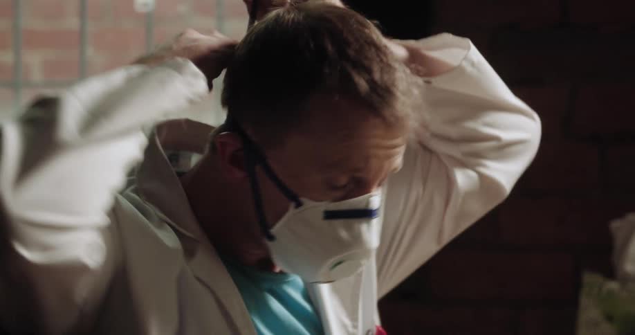 A man is putting on a face mask while sitting indoors