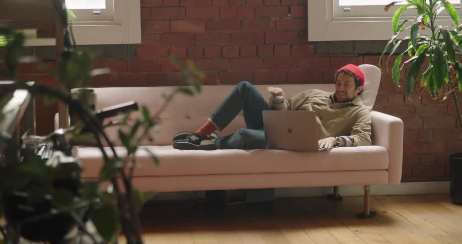 A man laying on a couch looking at a laptop