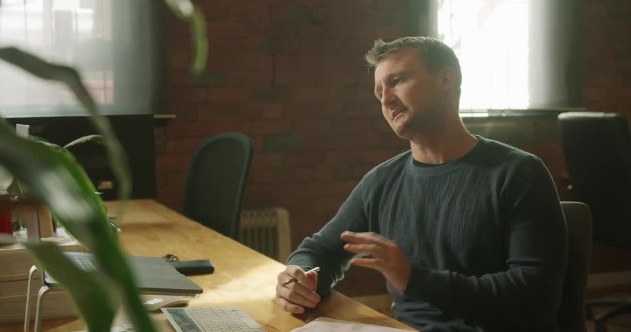 A man sits at a desk with a laptop having a video call
