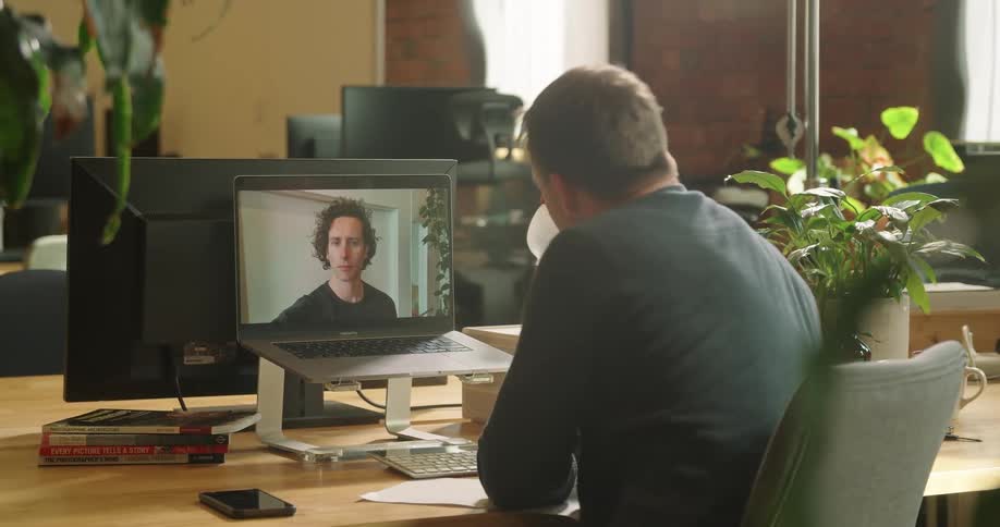 Two white men converse through a computer