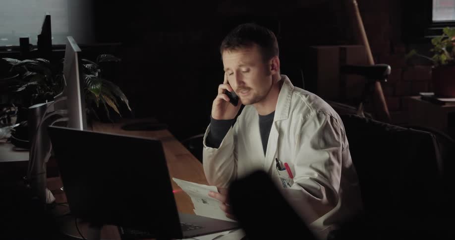 A man talks on the phone while looking at his computer screen and papers