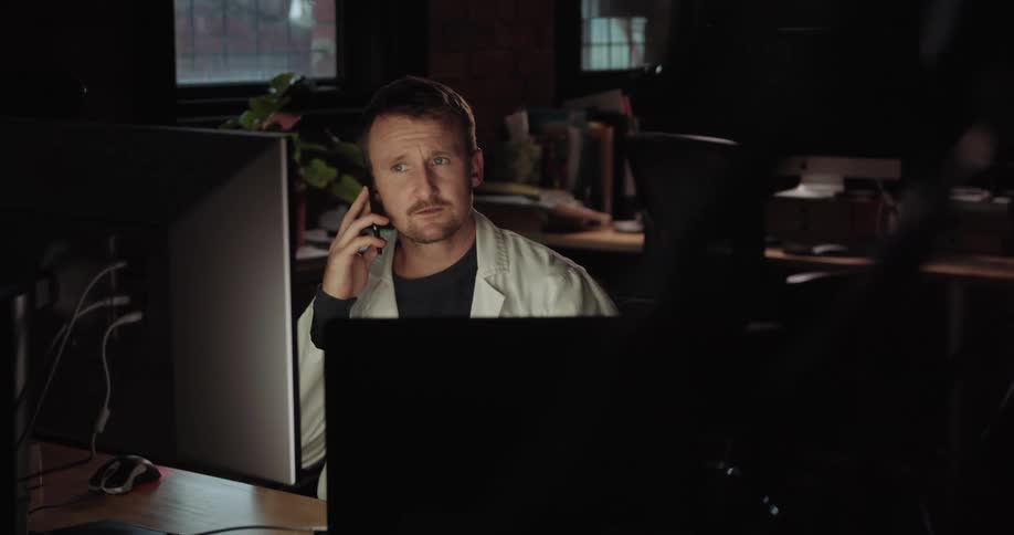 A man talks on the phone while looking at his computer