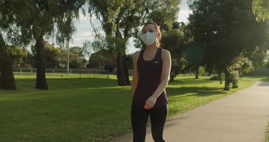 A woman wearing a medical mask walks down a path through a park