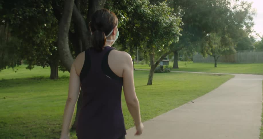 A woman wearing a mask walks along a path