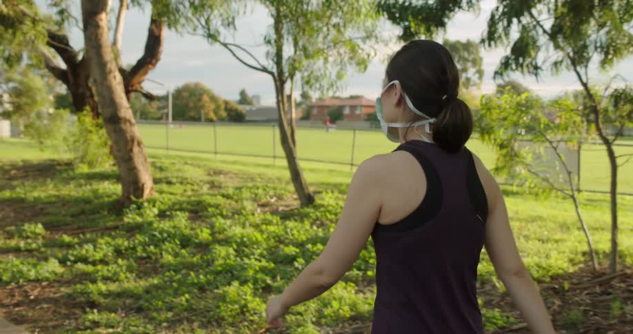 Woman walks through park past sports fields and trees