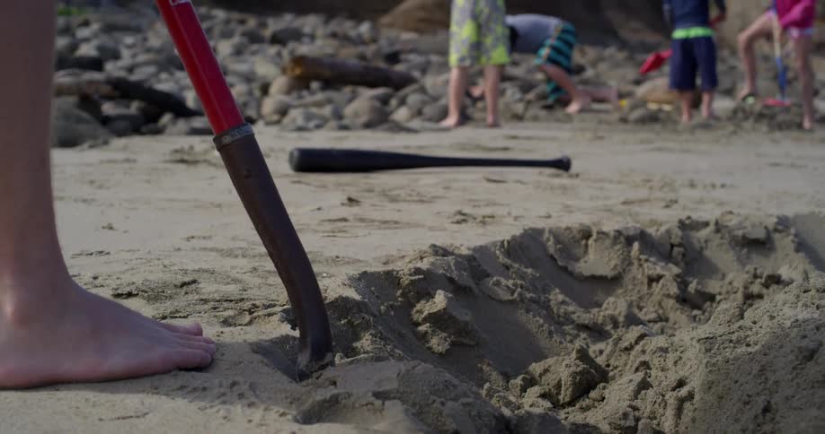 A person moves sand with a shovel while children play nearby