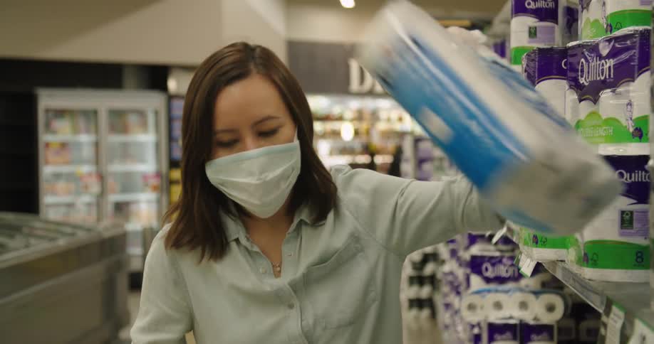 A woman in a mask shops for toilet paper
