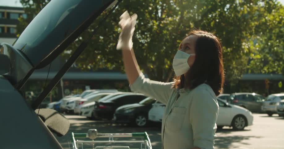 A woman wearing a mask loads groceries in to her car