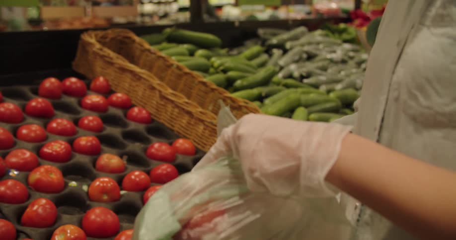 A person puts tomatoes in a plastic bag at a grocery store