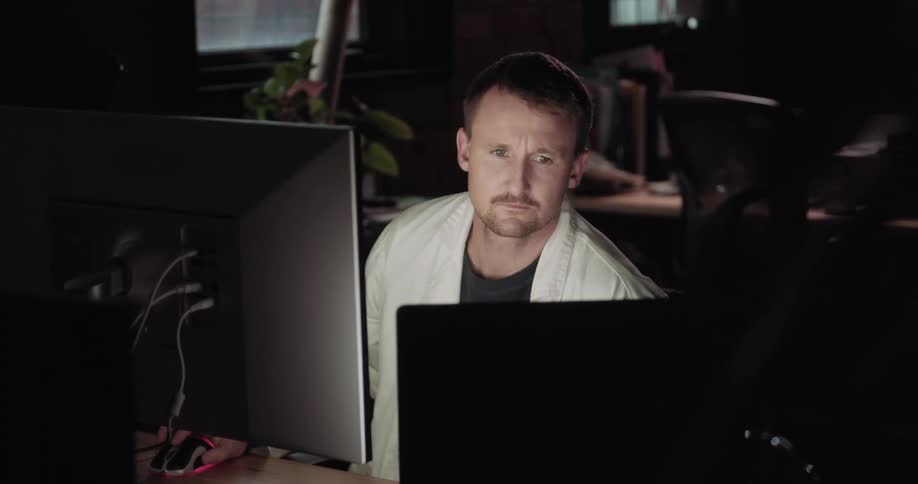 Man sits in dark empty shared office working on computer