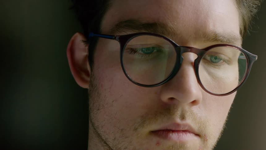 Man in round glasses looks down to read