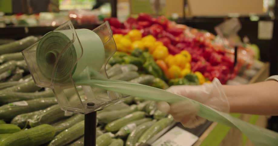 Person wearing gloves selects produce bag near produce in grocery store
