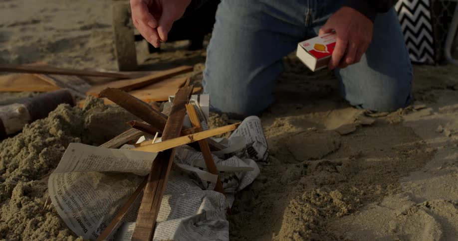 A man uses a match to light newspaper on fire as he starts a campfire