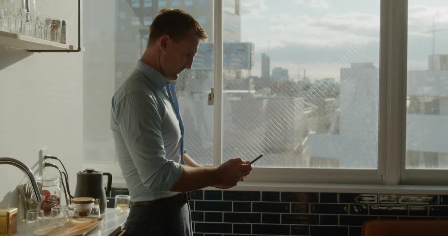 Man texting on cell phone near a window on kitchen