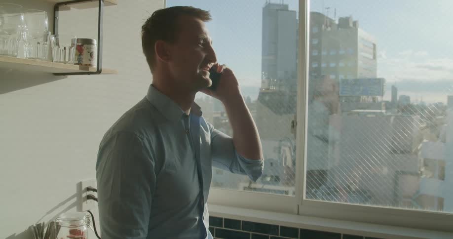 Man laughs while talking on mobile phone near window