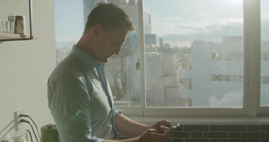 A man standing in a kitchen touching a smart phone