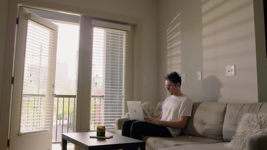 Man sitting on the sofa opens laptop and types in the living room