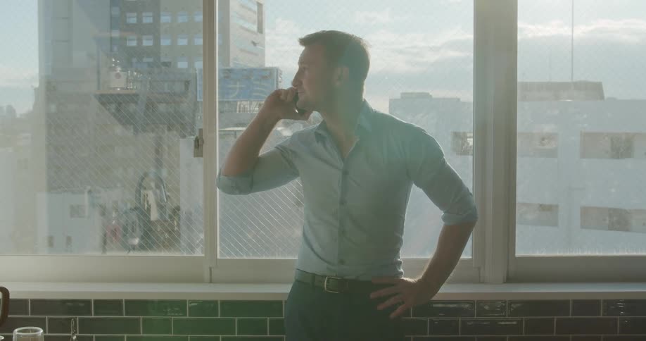 Man talks on cell phone near window in kitchen