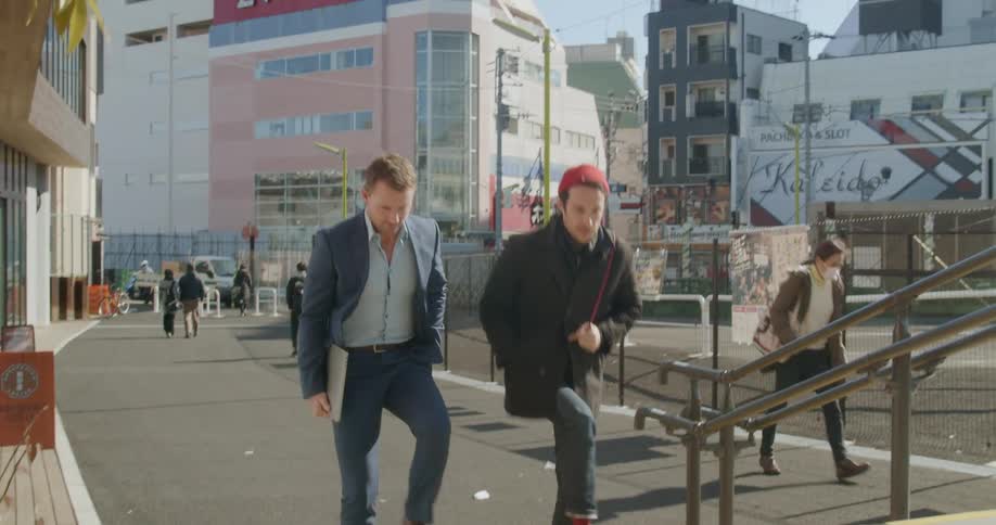 Two men talk as they walk down the city street on a sunny day