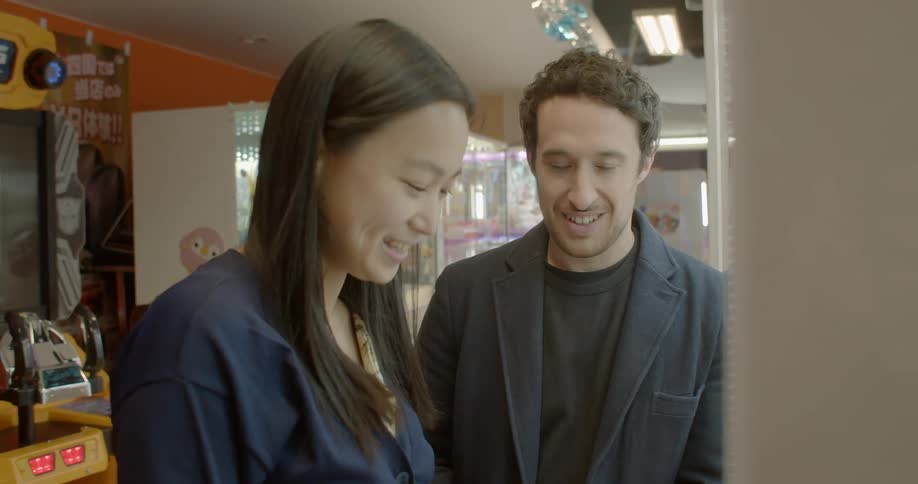 A man and woman stand next to an arcade game laughing