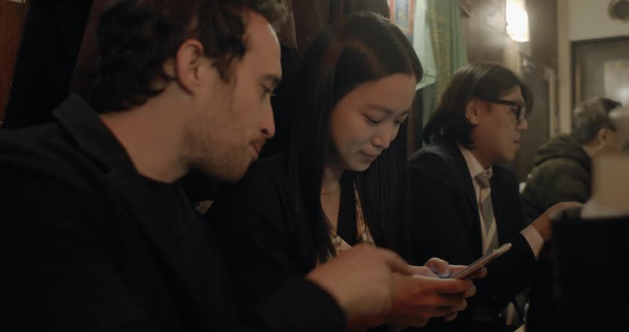 Asian woman and white man sitting at the table uses a smartphone in the cafe