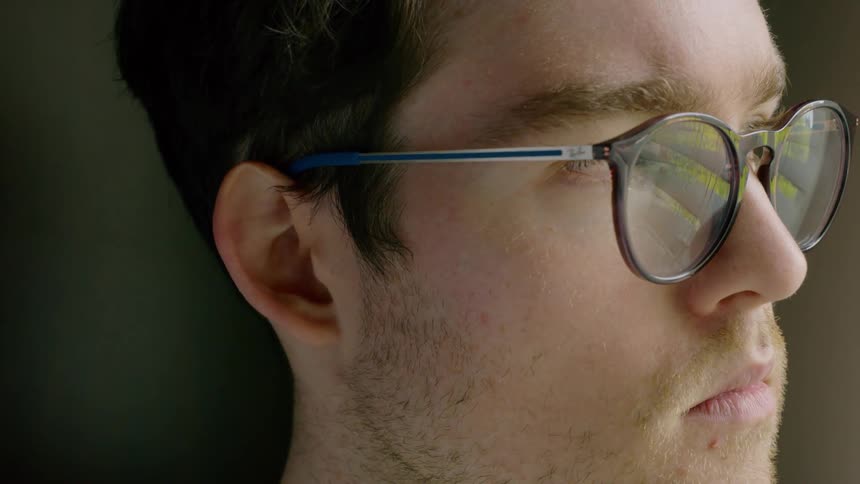A man wearing glasses looks down in front of him the turns his head and looks left
