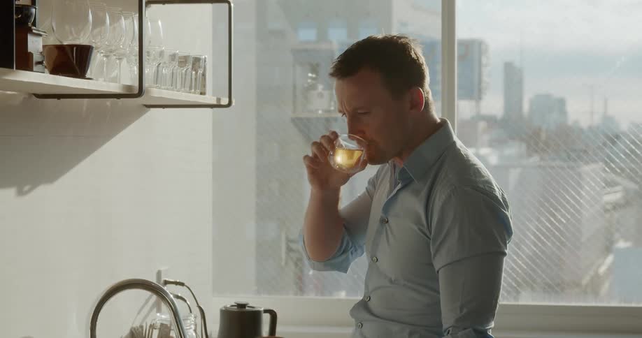A person types on a laptop while sipping a small drink