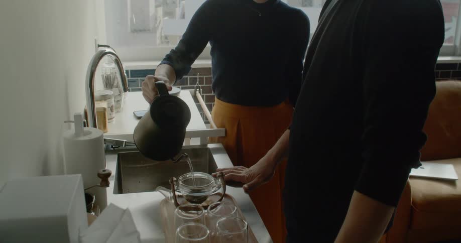 A woman pours hot water in to a tea pot as a man watches