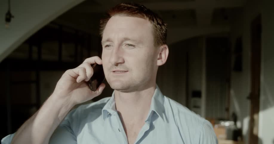 A man grinning while talking on a smartphone indoors