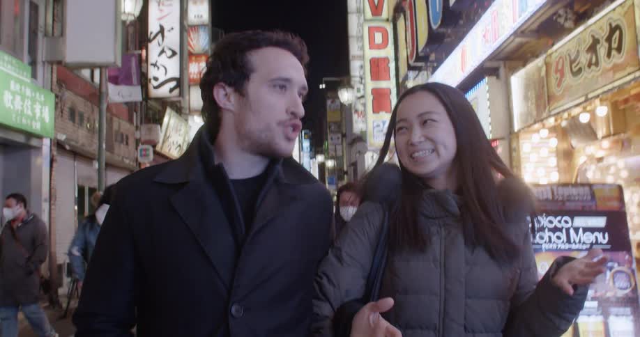 White man and asian woman walk down the street at night in the city