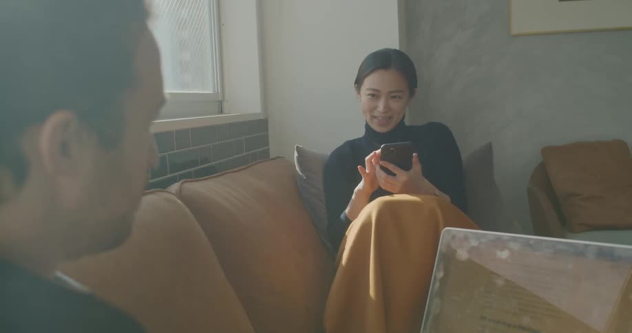 A man and woman talk while using their electronics on a sofa