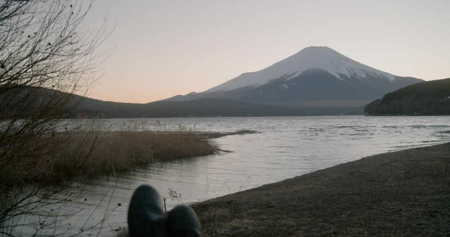 A person is sitting by the coast a mountain is in the distance