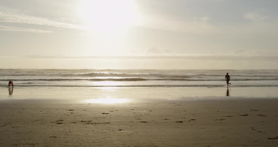 Two people run down a sandy beach