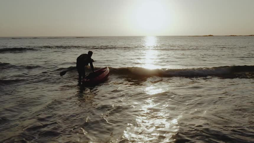Man gets into sea kayak on ocean at sunset