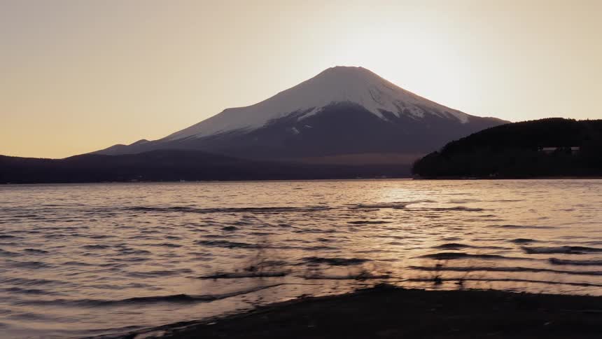 A mountain stands behind an ocean at sunrise