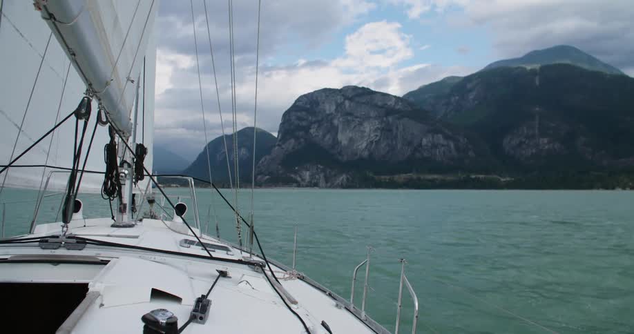 Sailboat on calm ocean waters in front of coastal mountains at day