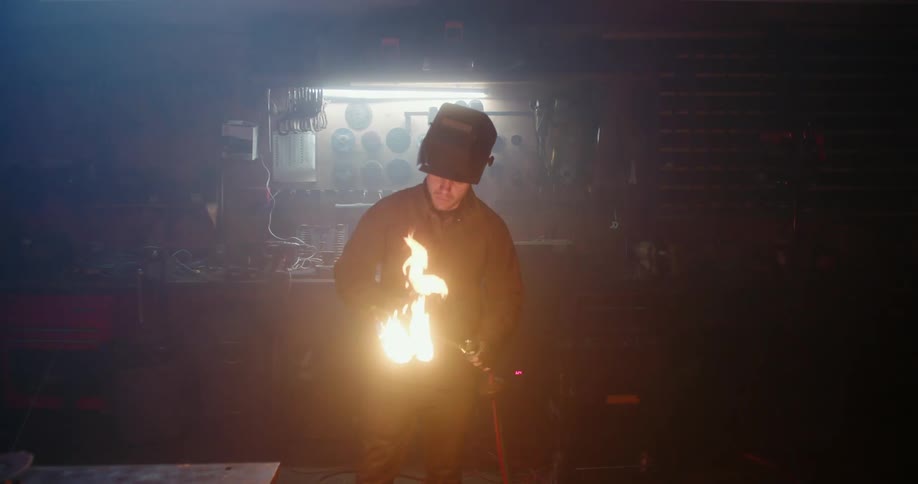 A welder lights his gas torch while standing in a dark workshop