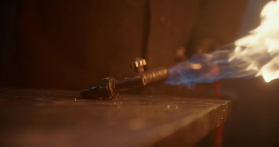 A person lights a gas torch in a dark workshop