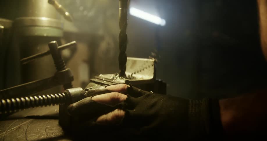 A person drills into metal in a dark work area