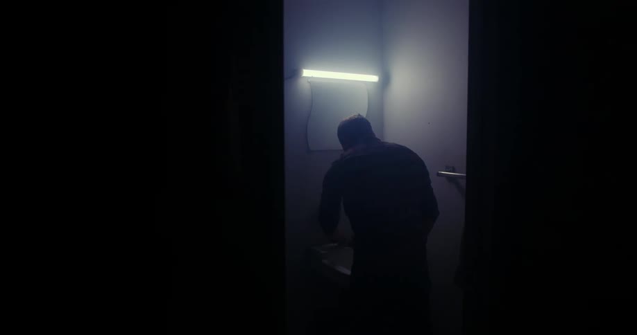 A person takes off a hat and goes into a dark restroom